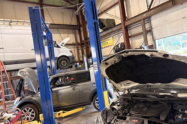 Inside the Kingdom Auto shop: two blue lifts, a van raised for service, a Mini and a Mercedes with hoods open